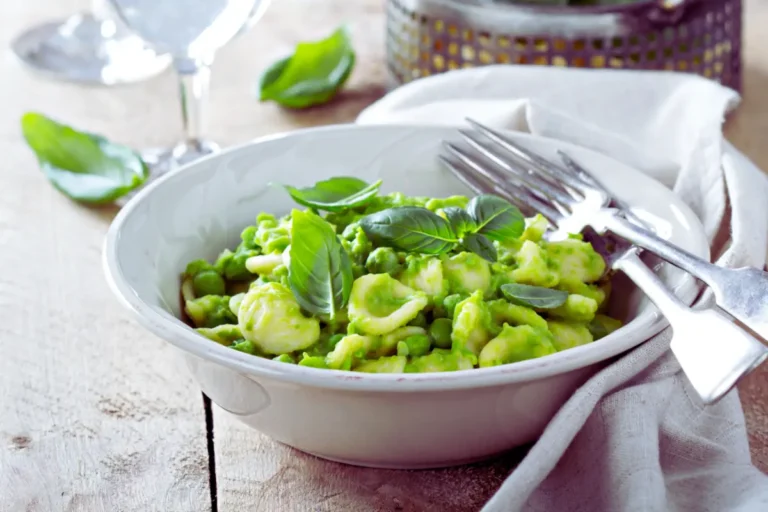 Orecchiette-Nudeln mit Erbsen in grüner Sauce, garniert mit Basilikumblättern, serviert in einer weißen Schüssel.