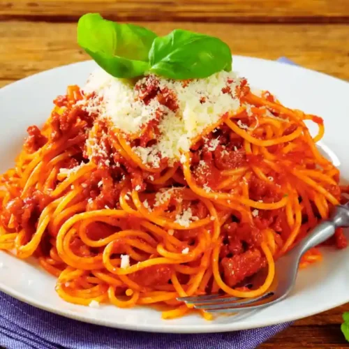 Pasta Pomodoro: Meistere den unwiderstehlichen Klassiker! 2 Spaghetti mit Tomatensoße, garniert mit geriebenem Käse und frischem Basilikum auf einem weißen Teller.