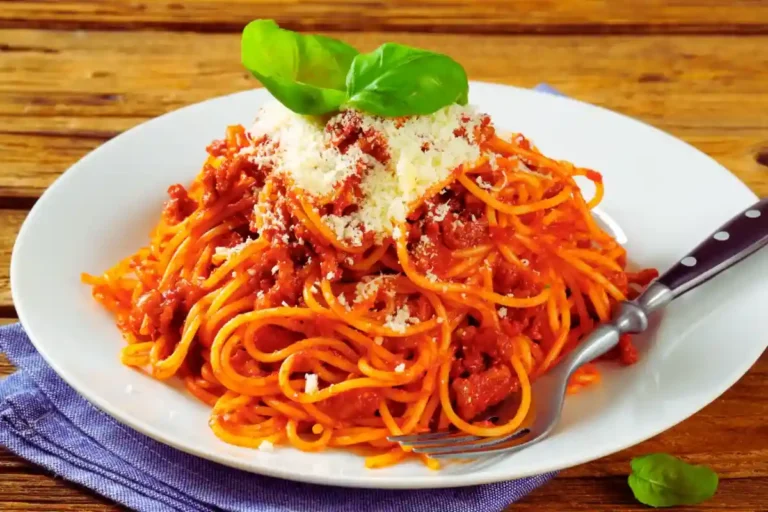 Spaghetti mit Tomatensoße, garniert mit geriebenem Käse und frischem Basilikum auf einem weißen Teller.